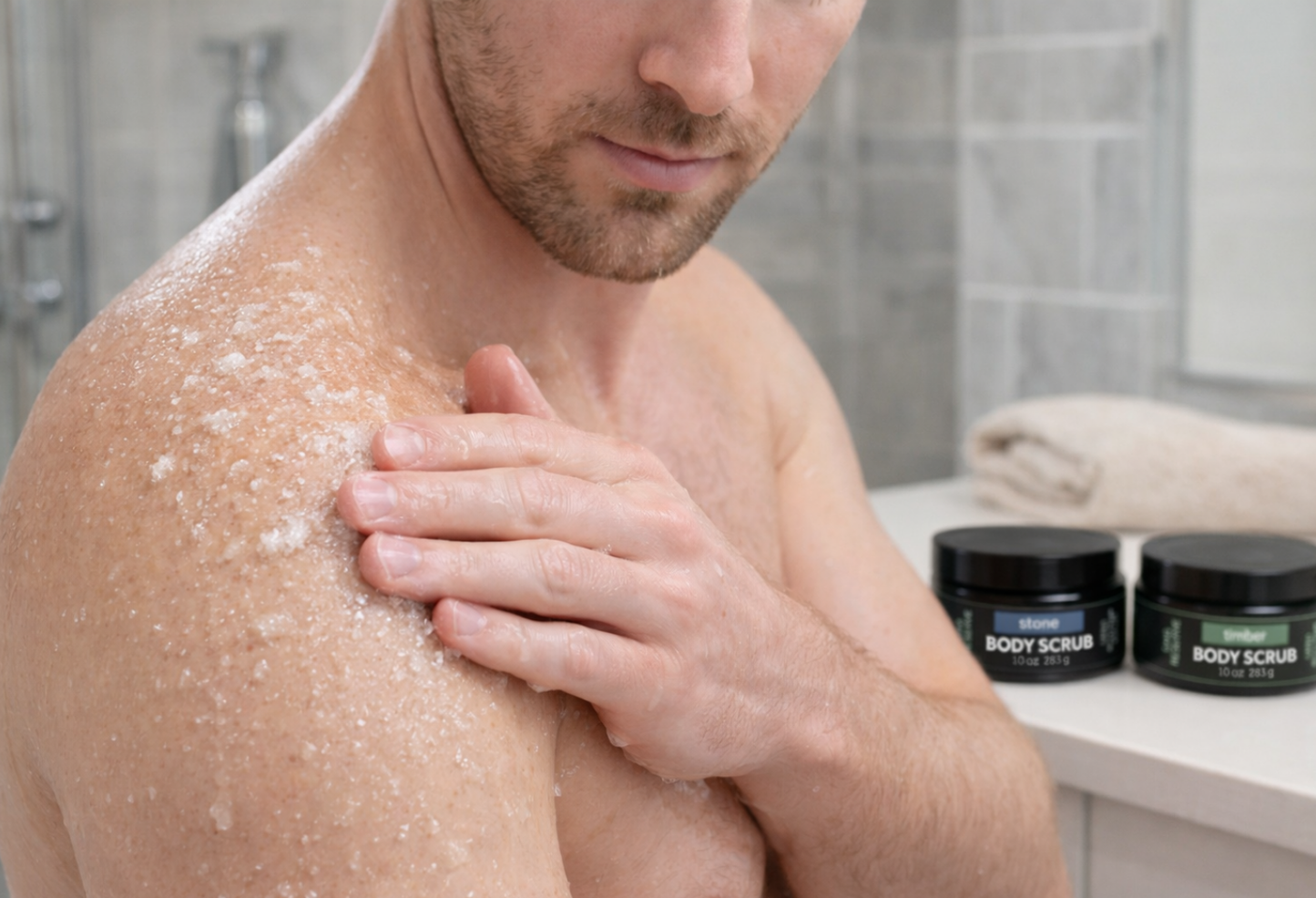 Man applying SMG Reserve exfoliating body scrub to his shoulder in a bathroom setting